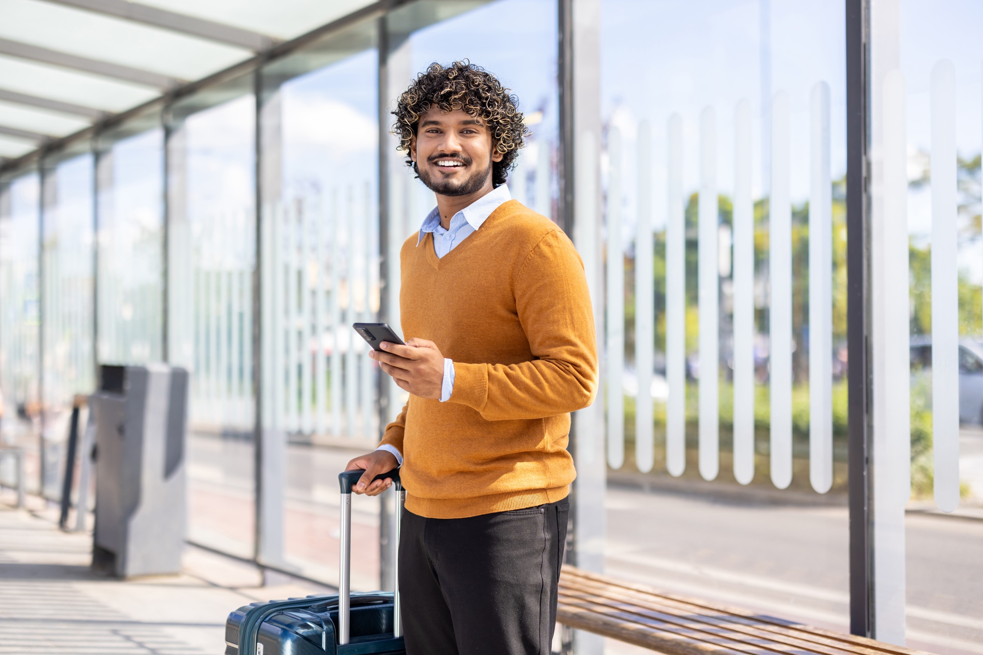 Portrait of a male passenger at a public transport stop, looking at the camera and smiling with a